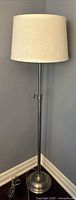 Full view of silver adjustable floor lamp with cream shade