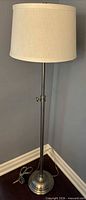 Full view of silver adjustable floor lamp with cream shade