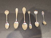 All six collector spoons side by side showing overall condition and size comparison