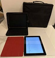 iPad 2 powered on with accessories: red cover, keyboard case open, black sleeve