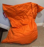 Front view of orange Fatboy bean bag folded against wall