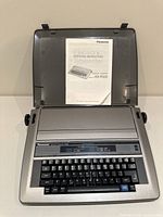 Typewriter open in travel case showing manual inside lid