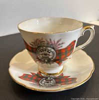 teacup on saucer showing clan crest, tartan ribbon, heather, gold trim