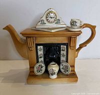 Front view of fireplace-shaped teapot with clock lid and decorative miniatures