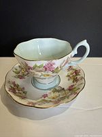 teacup on saucer showing exterior floral pattern, pale aqua interior and gold trim