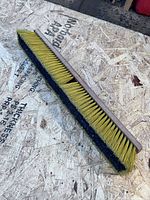 Top view of 24 in. wooden push broom head showing yellow and black bristles