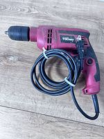 Full view left side of red Hyper Tough hammer drill with wrapped cord