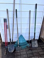 All seven garden tools leaning against exterior wall