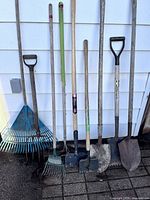 Nine long-handled garden tools lined up against wall