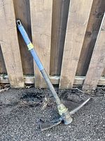 Full view of pick mattock leaning against fence
