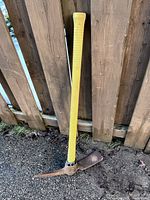 Full view of pick mattock leaning against fence