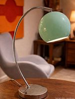 Side view of lamp on table, chrome arc, mint globe shade, base visible