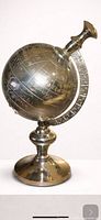 Front view of silver-tone metal globe showing engraved continents and pedestal base