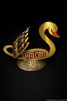 Front view of brass swan figurine showing enamel lettering and base relief