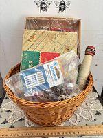 Overall view of wicker basket with contents: Singer attachment box, bag of bobbins, needles pack, wooden spool