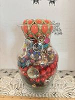 Full view of glass vase filled with assorted jewelry