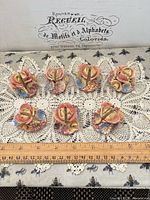 Seven porcelain floral place card holders on lace cloth with ruler for scale