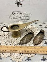 Brass incense burner and two brass shoe ashtrays on doily with ruler for scale