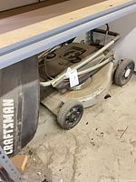 Craftsman push mower under shelf showing wheels, deck, handle