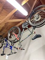 Two inverted bicycles hanging from ceiling, side view showing frames, wheels, drivetrains