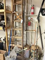 Two wooden ladders leaning with surrounding cleaning tools and hardware visible