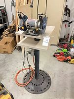 Full view of bench grinder on pedestal stand with power cord