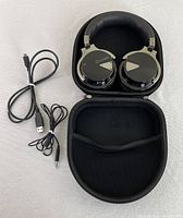 Headphones in open case with charging and audio cables beside