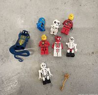 Group of LEGO Ninjago minifigure parts and staff on grey surface