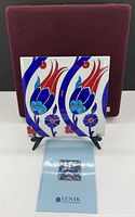Front view of porcelain tile on easel, showing Iznik tulip design and certificate booklet