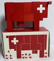 Assembled red wooden cow puzzle displayed atop original box