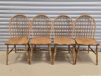Group shot of four matching natural wood Windsor spindle back dining chairs