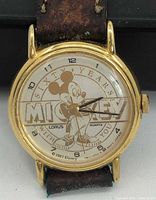 Close-up of watch dial showing Mickey Mouse 60th anniversary design and gold-tone case