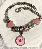 Close-up of bracelet showing chain, clasp, and charms including pink crown disc