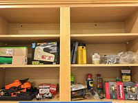 Cabinet shelves showing staple gun, flashlight, sprays, earmuffs and hardware
