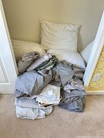 Pile of assorted sheets and two pillows in closet alcove