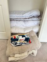 stacked white duvets in closet with beige and colorful throws