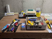 Wide view of table with paint tray, roller, brushes, clamps, caulk tubes, tools