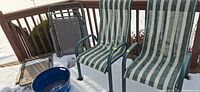 Full view of two sling chairs, blue bucket in foreground, folded bucket not showing internal, snow background
