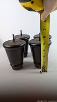 Four tapered dark wood furniture legs shown with tape measure indicating height ~4.5-5 in.