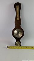 Full view of wooden banjo-style barometer with ruler for scale