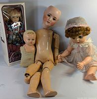 Group shot of all four dolls including boxed porcelain doll, jointed bisque doll, plastic baby doll and small cloth baby doll