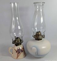 Both ceramic oil lamps with glass chimneys side by side