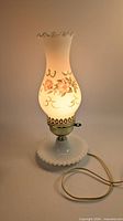Full view of lit milk glass hurricane lamp showing floral chimney and hobnail base