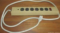 Top view of beige metal power bar showing six black outlets and white cord
