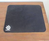 Top view of black SteelSeries QcK mouse pad on wooden surface