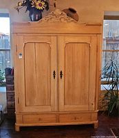 Front view of light oak solid wood armoire with carved crest, double doors and two drawers