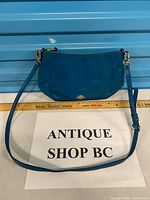 Front view of blue Coach leather crossbody bag with strap and measuring tape showing width about 30 cm