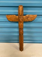 Front view of full totem sculpture showing eagle wings and stacked faces