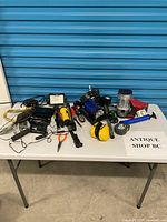 Overview of lot on table showing flashlights, work light, lantern, ear muffs, lanyard, router and accessories