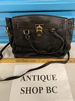 Front view of black leather Michael Kors handbag showing padlock, handles, strap